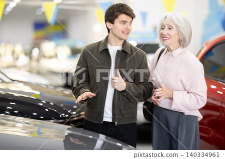 Adult son helps her elderly mother choose a new car at car dealership Adult son helps her elderly mother choose a new car at car dealership 140334961
