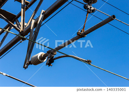 Close-up of railway overhead wires, low-angle shot looking up, against a blue sky background. 140335001