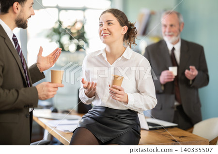 Young woman and man co-worker employees drinking coffee and talking during break while working in office Young woman and man co-worker employees drinking coffee and talking during break while working in office 140335507