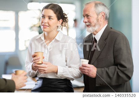 Young woman and man co-worker employees drinking coffee and talking during break while working in office Young woman and man co-worker employees drinking coffee and talking during break while working in office 140335520