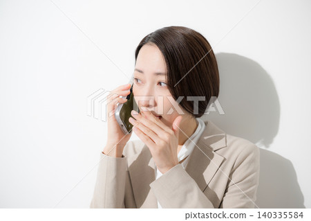 A close-up of a businesswoman in a suit who is troubled and worried about secretly having an inappropriate conversation on her smartphone. 140335584