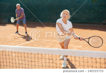 Elderly playing tennis together in court Elderly playing tennis together in court 140335733