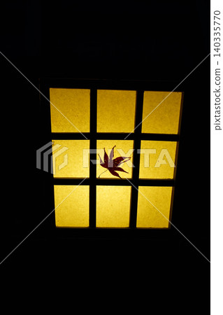 Maple leaves clinging to a lit lantern Maple leaves clinging to a lit lantern 140335770