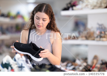 Young woman in casual clothes chooses pair of sneakers in shoe store Young woman in casual clothes chooses pair of sneakers in shoe store 140335778