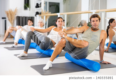 Middle-aged man practicing pilates with roller on gray mat in gym room Middle-aged man practicing pilates with roller on gray mat in gym room 140335891