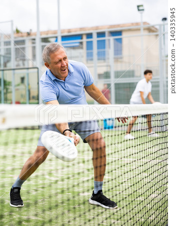 Unusual angle through tennis net on an elderly male padel player Unusual angle through tennis net on an elderly male padel player 140335945