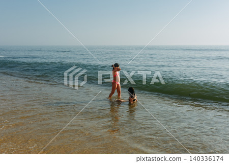 Two Young Girls Playing in Gentle Ocean Waves on Sunny Summer Beach Day Two Young Girls Playing in Gentle Ocean Waves on Sunny Summer Beach Day 140336174
