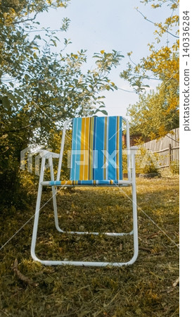 Blue and Yellow Striped Deck Chair in Garden with Trees and Grass Blue and Yellow Striped Deck Chair in Garden with Trees and Grass 140336284