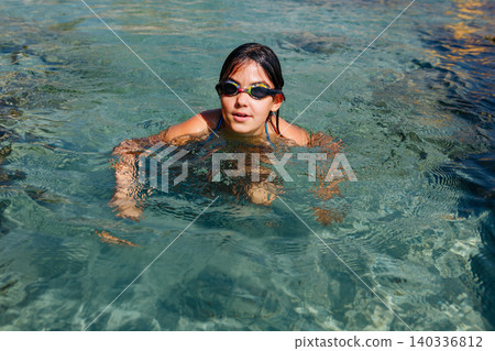 young girl swimming in the blue sea with coloured goggles 140336812