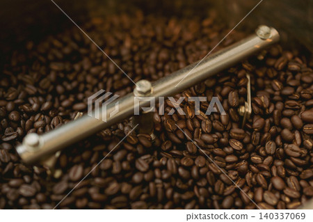 Dark roast coffee beans being rotated and stirred on a cooling plate in a roaster. (Image showing the roasting process.) 140337069