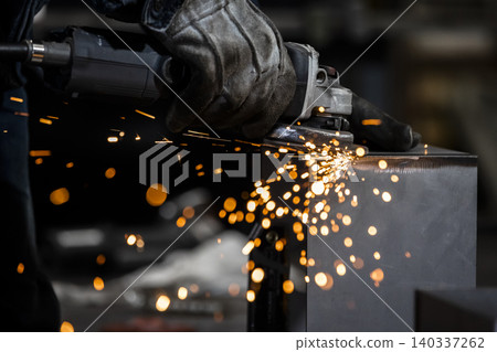 A close-up of a craftsman's hands as he grinds the edges of metal with a disc grinder, sending sparks flying. A close-up of a craftsman's hands as he grinds the edges of metal with a disc grinder, sending sparks flying. 140337262