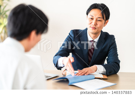 一位身穿西裝的商人面帶微笑地解釋著建築合約。 一位身穿西裝的商人面帶微笑地解釋著建築合約。 140337883