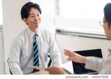 A man in a dress shirt receives instructions from a staff member in charge of work uniforms in the office. A man in a dress shirt receives instructions from a staff member in charge of work uniforms in the office. 140337889