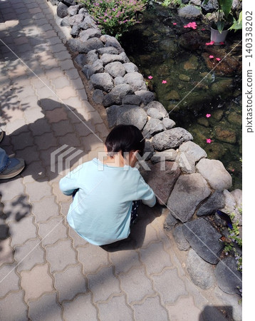 The back view of a boy sitting down and picking up stones. The back view of a boy sitting down and picking up stones. 140338202