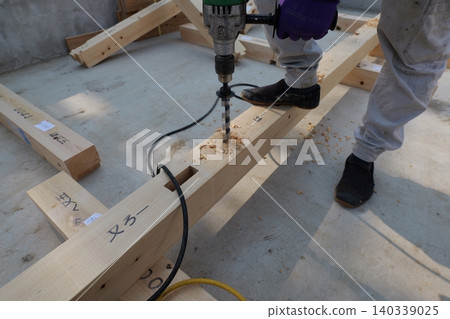 Japanese carpenter drilling holes in wooden foundation beam at construction site 140339025