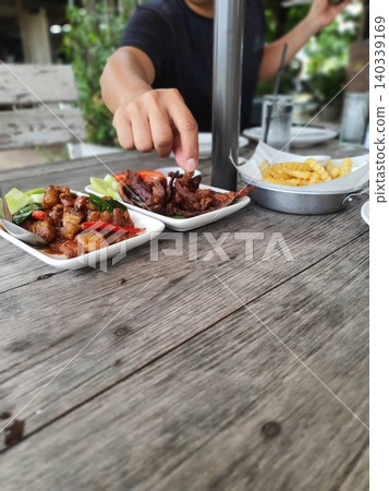 Close up of a man's hand picking food on a wooden table at an outdoor restaurant. Close up of a man's hand picking food on a wooden table at an outdoor restaurant. 140339169
