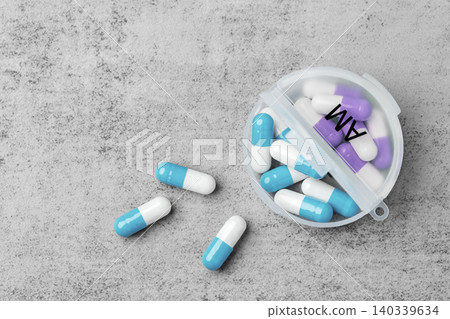 Pills spilling with open daily pill organizer on a grey concrete background, top view Pills spilling with open daily pill organizer on a grey concrete background, top view 140339634
