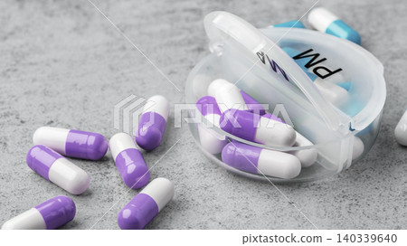 Purple and white capsule pills scattered around with opened daily pill box on a grey concrete surface Purple and white capsule pills scattered around with opened daily pill box on a grey concrete surface 140339640