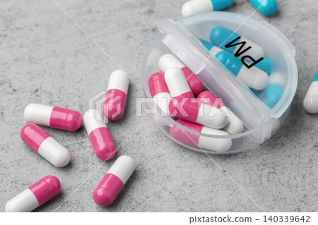 Capsule pills scattered around with opened daily pill box on a grey concrete background Capsule pills scattered around with opened daily pill box on a grey concrete background 140339642