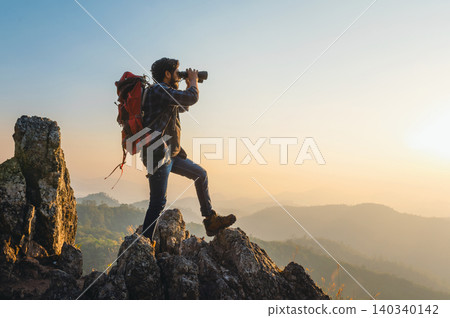 Hiker stands atop rugged peak at golden sunrise Hiker stands atop rugged peak at golden sunrise 140340142