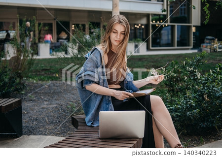 Woman working next to laptop on wooden public bench. university student homework, learning outside classroom, upskilling professional courses. Woman working next to laptop on wooden public bench. university student homework, learning outside classroom, upskilling professional courses. 140340223