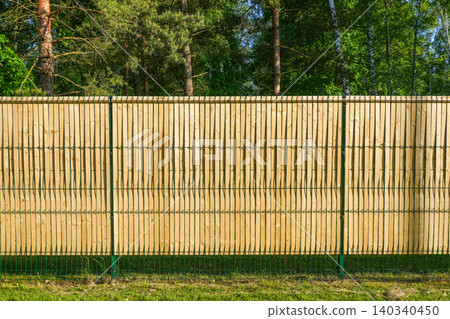 Wooden privacy slats integrated into green welded mesh fence along forest property boundary line 140340450
