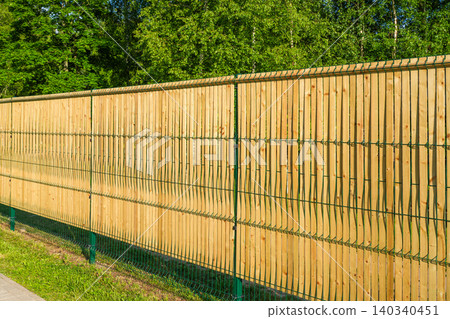 Wooden privacy slats installed in green welded wire mesh fence along landscaped property boundary Wooden privacy slats installed in green welded wire mesh fence along landscaped property boundary 140340451