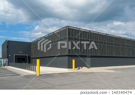 Modern industrial warehouse building with metal facade and empty parking area under dramatic sky Modern industrial warehouse building with metal facade and empty parking area under dramatic sky 140340474