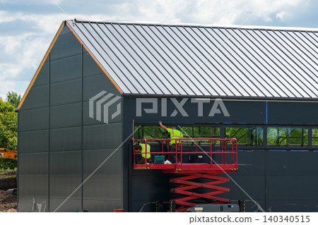 Workers installing facade panels on modern industrial building using scissor lift platform equipment Workers installing facade panels on modern industrial building using scissor lift platform equipment 140340515
