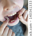 A 10-year-old boy shows a fresh empty socket in his lower jaw after losing a baby tooth. He holds the shed milk tooth in his hand, highlighting natural childhood development and dental growth. A 10-year-old boy shows a fresh empty socket in his lower jaw after losing a baby tooth. He holds the shed milk tooth in his hand, highlighting natural childhood development and dental growth. 140341333