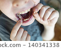 A 10-year-old boy shows a fresh empty socket in his lower jaw after losing a baby tooth. He holds the shed milk tooth in his hand, highlighting natural childhood development and dental growth. A 10-year-old boy shows a fresh empty socket in his lower jaw after losing a baby tooth. He holds the shed milk tooth in his hand, highlighting natural childhood development and dental growth. 140341338