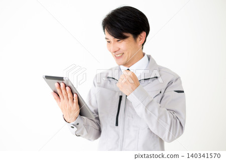 A middle-aged businessman in gray work clothes makes a triumphant gesture while looking at a tablet against a white background. A middle-aged businessman in gray work clothes makes a triumphant gesture while looking at a tablet against a white background. 140341570