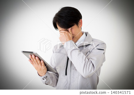 A middle-aged businessman in gray work clothes looks dejected while looking at a tablet against a white background. 140341571