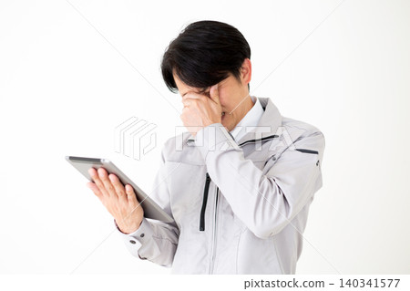 A middle-aged businessman in gray work clothes looks dejected while looking at a tablet against a white background. A middle-aged businessman in gray work clothes looks dejected while looking at a tablet against a white background. 140341577