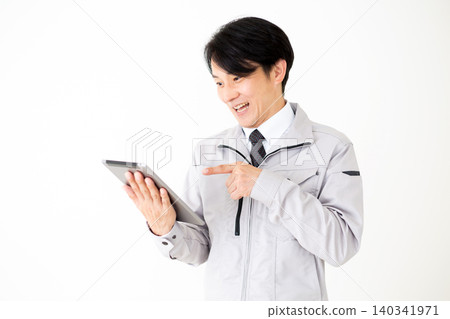 A middle-aged businessman in gray work clothes looks surprised while looking at a tablet, against a white background. A middle-aged businessman in gray work clothes looks surprised while looking at a tablet, against a white background. 140341971