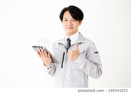 A middle-aged businessman in gray work clothes gives a thumbs-up while looking at a tablet against a white background. A middle-aged businessman in gray work clothes gives a thumbs-up while looking at a tablet against a white background. 140341972