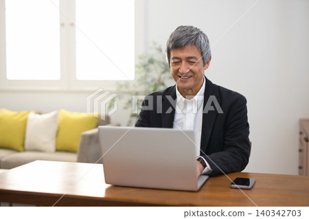 A man in his 60s wearing a jacket working on a laptop. A man in his 60s wearing a jacket working on a laptop. 140342703
