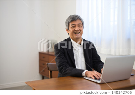 一位六十多歲的男子，穿著夾克，正在使用筆記型電腦。 140342706