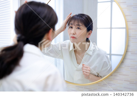 照鏡子時,會擔心自己髮際線後移的老年女性 照鏡子時,會擔心自己髮際線後移的老年女性 140342736
