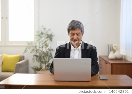 A man in his 60s wearing a jacket working on a laptop. A man in his 60s wearing a jacket working on a laptop. 140342801