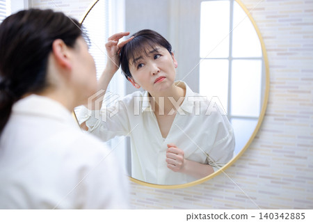 照鏡子時,會擔心自己髮際線後移的老年女性 照鏡子時,會擔心自己髮際線後移的老年女性 140342885