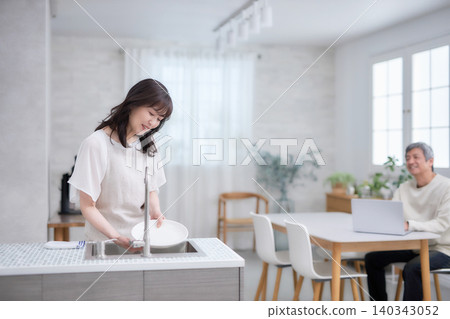 A man and woman in their 60s smiling and talking while wiping dishes in the kitchen A man and woman in their 60s smiling and talking while wiping dishes in the kitchen 140343052