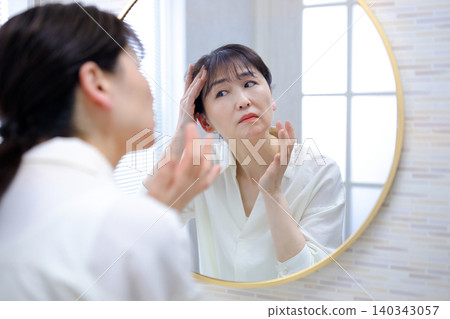 照鏡子時,會擔心自己髮際線後移的老年女性 照鏡子時,會擔心自己髮際線後移的老年女性 140343057