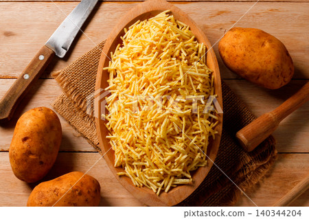 Gourmet portion of crispy fried yellow potato sticks in a rustic wooden bowl on a jute table Gourmet portion of crispy fried yellow potato sticks in a rustic wooden bowl on a jute table 140344204