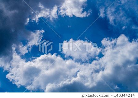 A view of white clouds against a blue sky, with the light from the sun shining through between fluffy mass 140344214