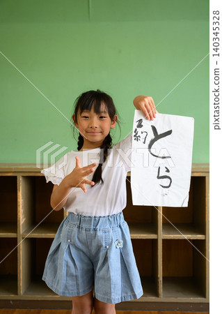 教室後方,一名小學生面帶微笑,舉起她用書法寫成的「老虎」字作品。 教室後方,一名小學生面帶微笑,舉起她用書法寫成的「老虎」字作品。 140345328
