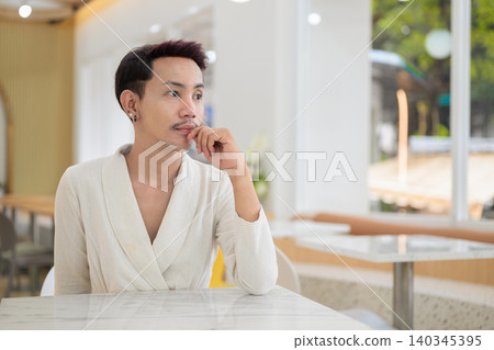Thoughtful non-binary gay Thai man looking away while sitting at a cafe table Thoughtful non-binary gay Thai man looking away while sitting at a cafe table 140345395