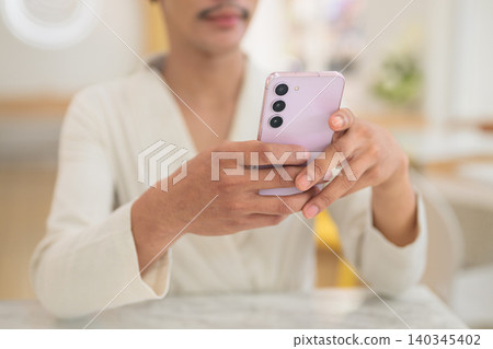 Close up of hands of non-binary gay Thai man typing on smartphone at modern cafe table Close up of hands of non-binary gay Thai man typing on smartphone at modern cafe table 140345402