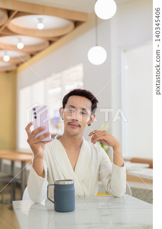 Vertical portrait of non-binary gay Thai man looking at smartphone with coffee mug at cafe table Vertical portrait of non-binary gay Thai man looking at smartphone with coffee mug at cafe table 140345406