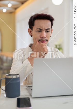 Vertical close up portrait of confused non-binary gay Thai man frowning at laptop screen at cafe Vertical close up portrait of confused non-binary gay Thai man frowning at laptop screen at cafe 140345429